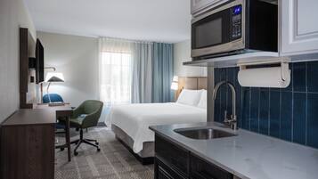 A hotel room with a bed, a desk, a chair, a microwave, and a sink.