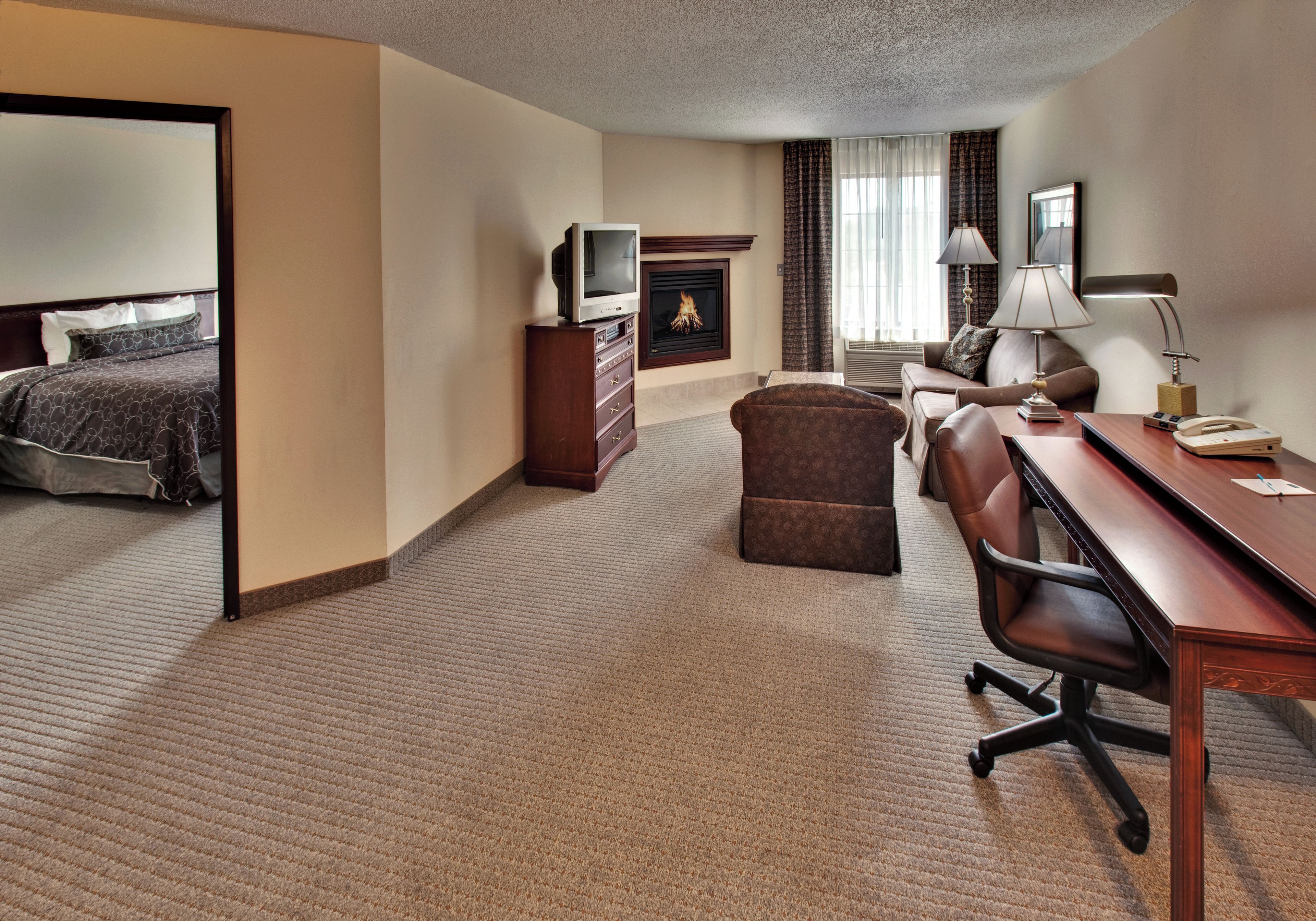 A hotel room with a bed, a desk, a chair, a television, a fireplace, and a window with curtains.