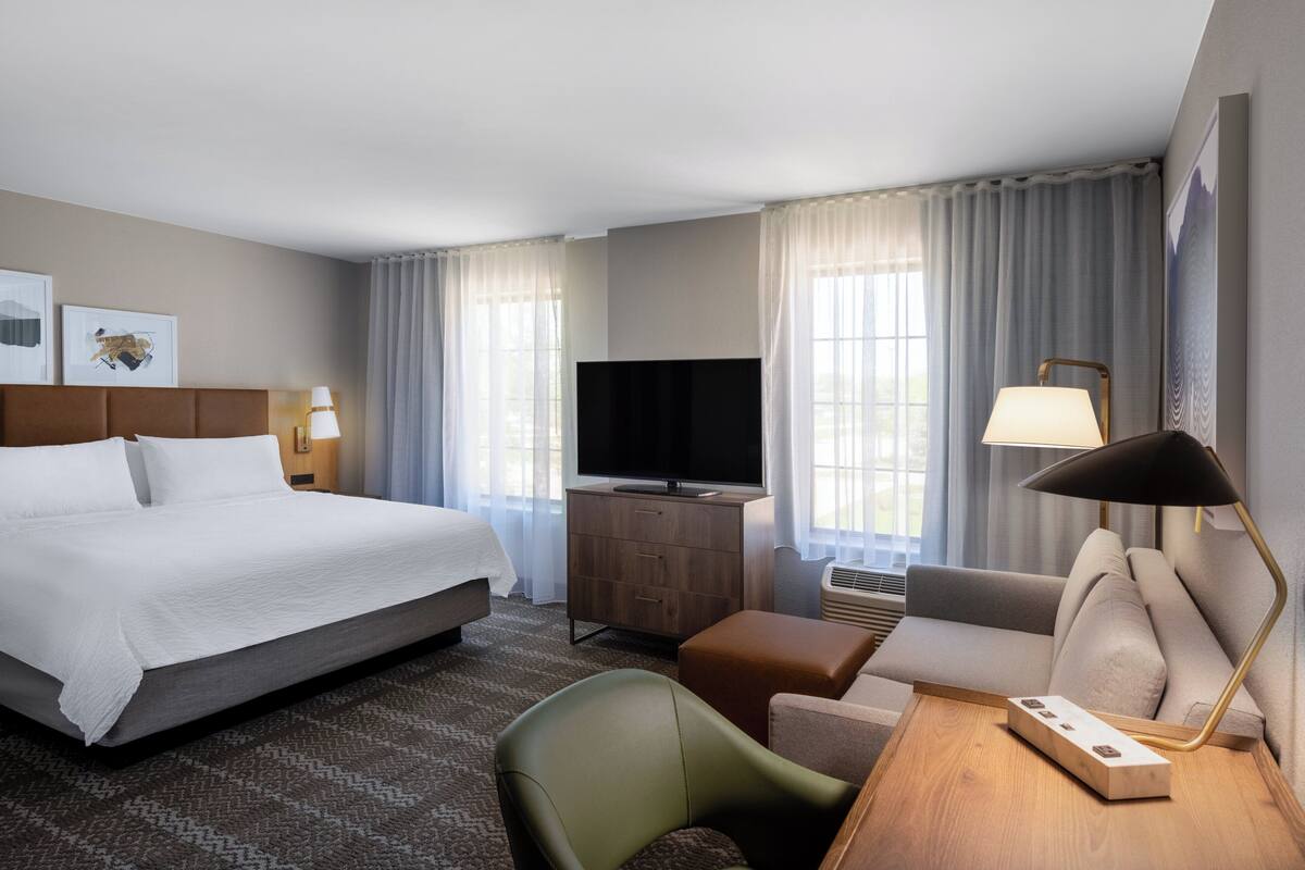 A hotel room with a large bed, a television, a desk with a lamp, a sofa, and a chair.