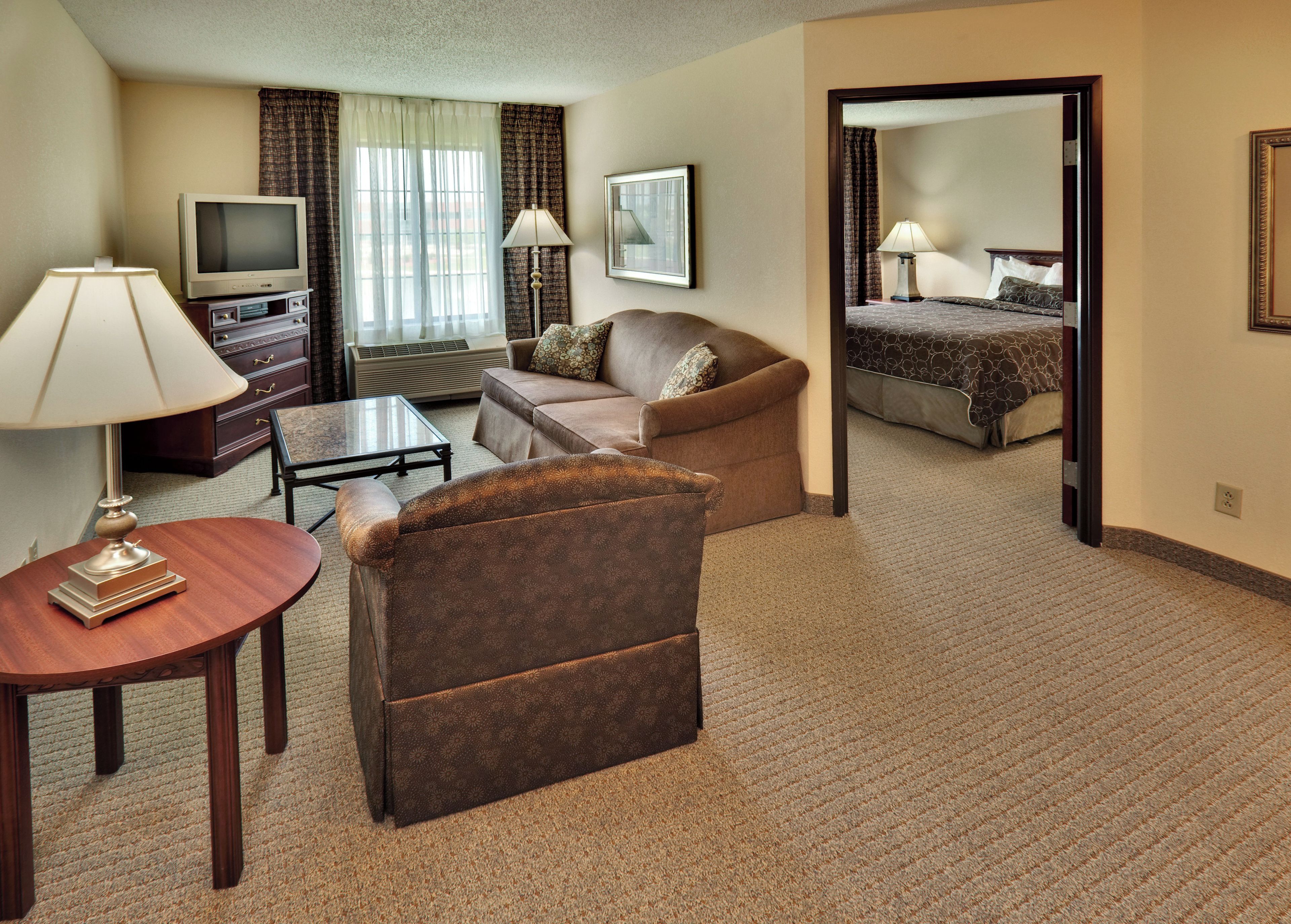 A hotel room with a sofa, armchair, television, and a bed with a patterned bedspread.