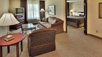 A hotel room with a sofa, armchair, television, and a bed with a patterned bedspread.