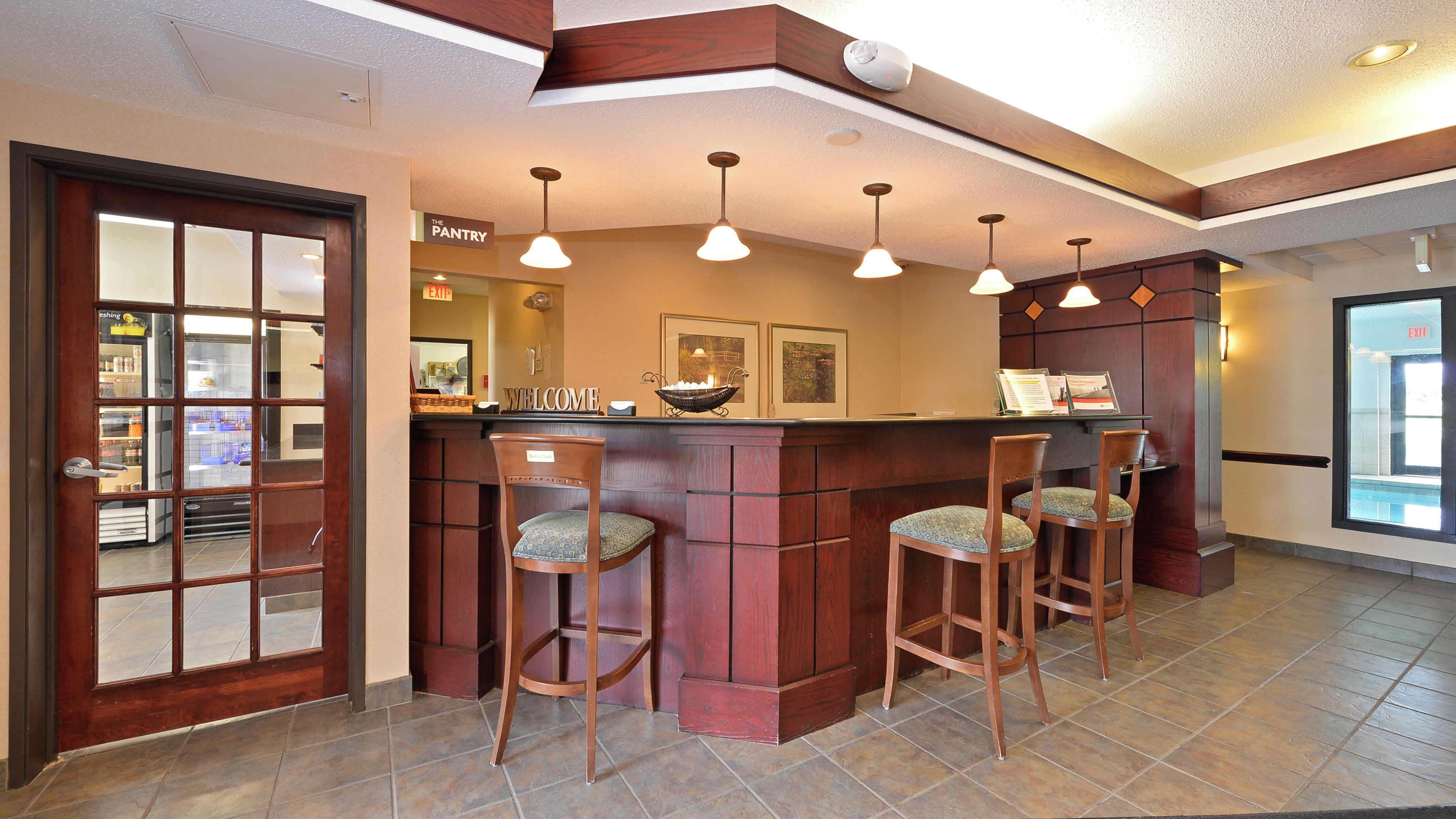 A bar area with a wooden counter, three bar stools, and pendant lighting.