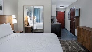 A hotel room with a large bed, a desk with a lamp, a wardrobe, a mirror, and a door leading to a bathroom. - Staybridge Suites West Des Moines by IHG (West Des Moines)