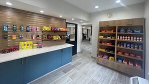 A clean, modern store interior with shelves stocked with snacks and beverages, a blue counter, and a wooden display unit. - Staybridge Suites West Des Moines by IHG (West Des Moines)