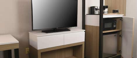 A modern hotel room with a flat-screen TV on a white cabinet, a microwave, and a coffee maker on a shelf.