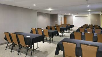 Un salón de conferencias con varias mesas y sillas, piso alfombrado e iluminación empotrada en el techo.