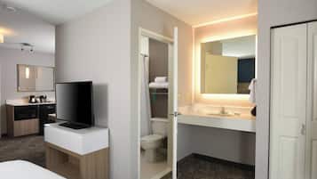 Een hotelbadkamer met een douche, toilet, wastafel en een televisie op een kast.