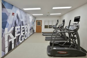Un gimnasio con cintas de correr, una pared decorativa y una puerta que da a otra sala.