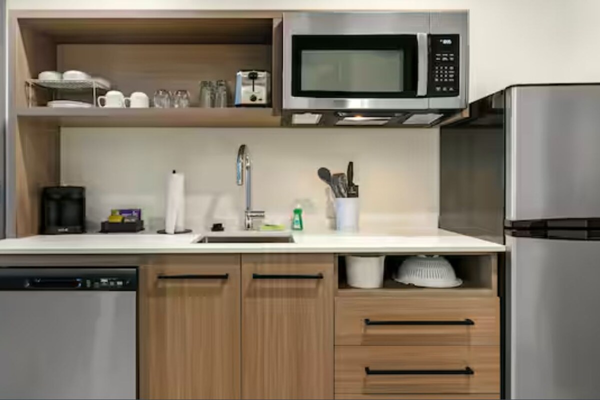 A modern kitchen with a dishwasher, microwave, refrigerator, wooden cabinets, and a sink.
