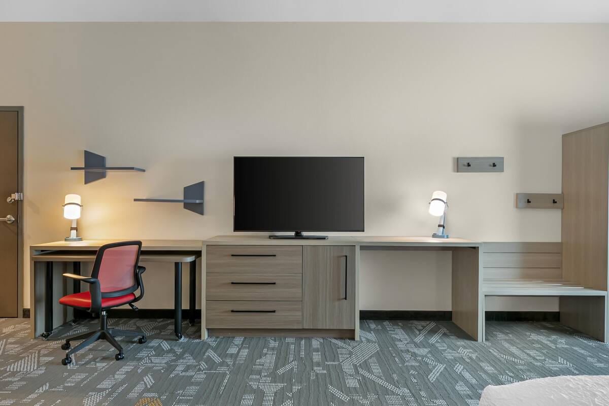 Habitación de hotel con escritorio, silla, televisor y cama.