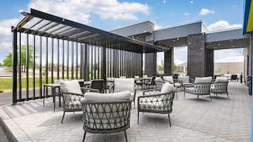 Un patio al aire libre con mobiliario de mimbre, una zona de estar cubierta y un edificio de ladrillo al fondo.