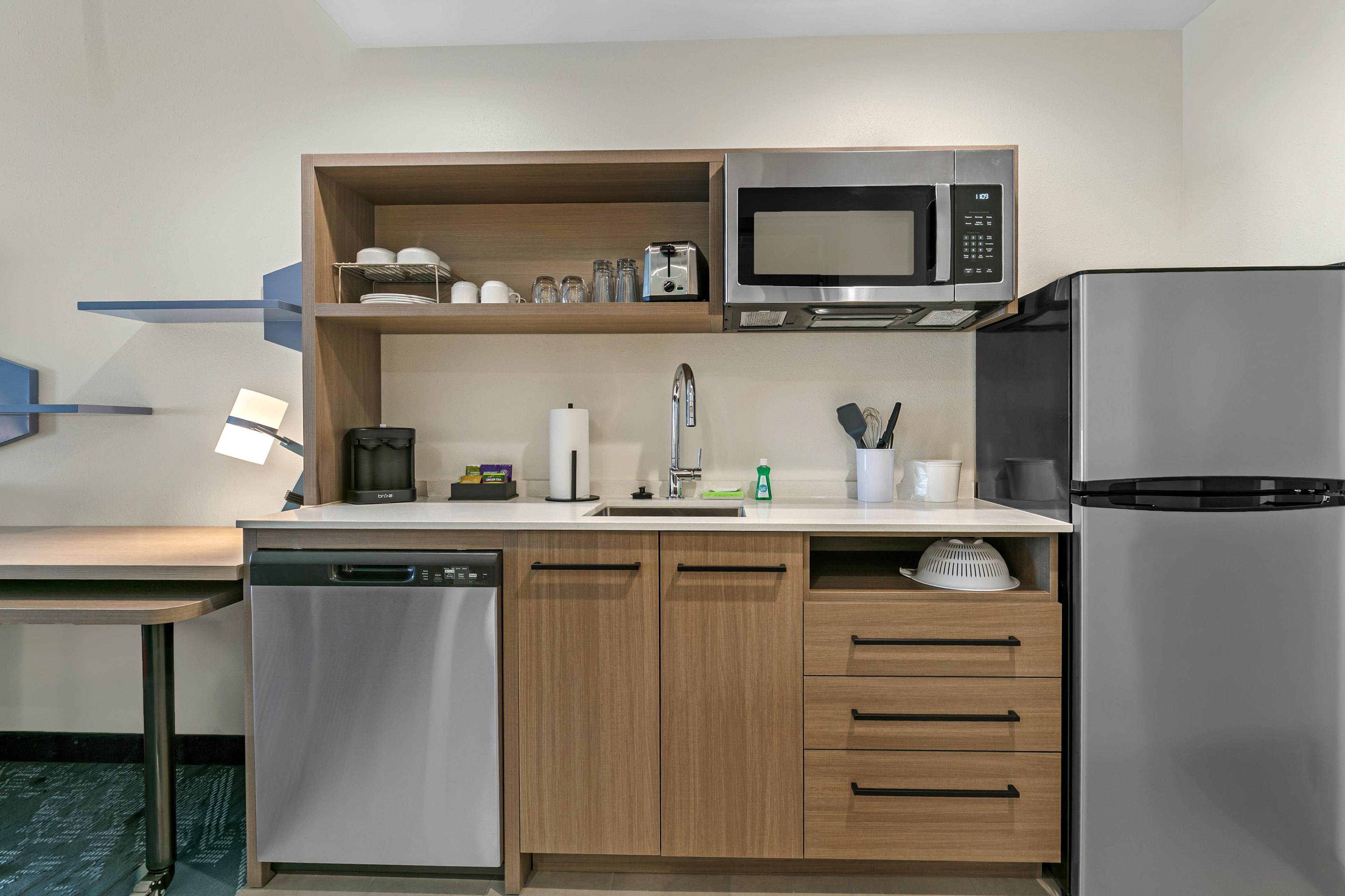 A modern kitchen with a dishwasher, microwave, refrigerator, and wooden cabinets.