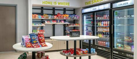 A snack display area with shelves of snacks, a table with snack packages, and two refrigerators labeled 'COLD' and 'COLDER'.