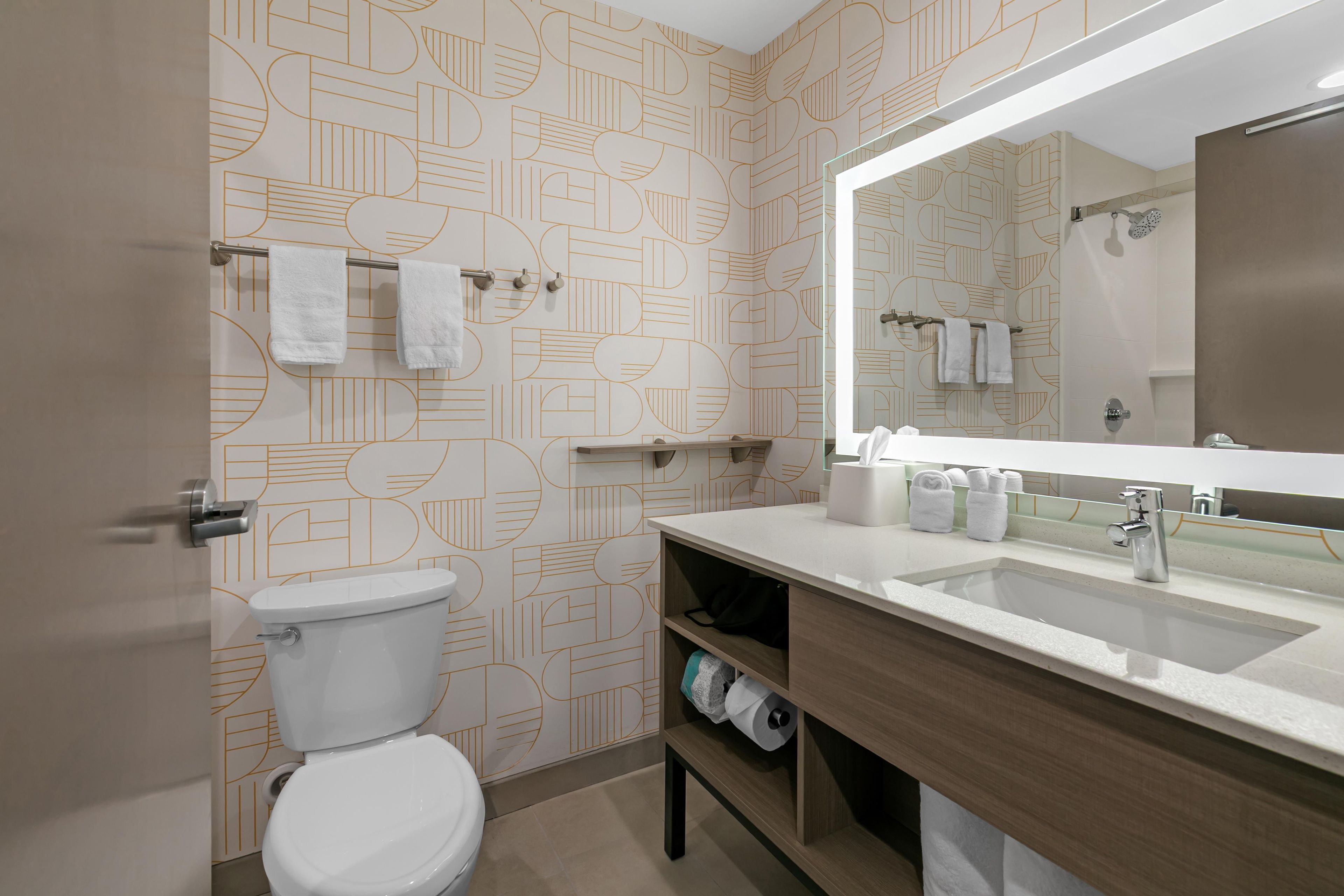 A bathroom with a toilet, a sink with a mirror, and patterned wallpaper.