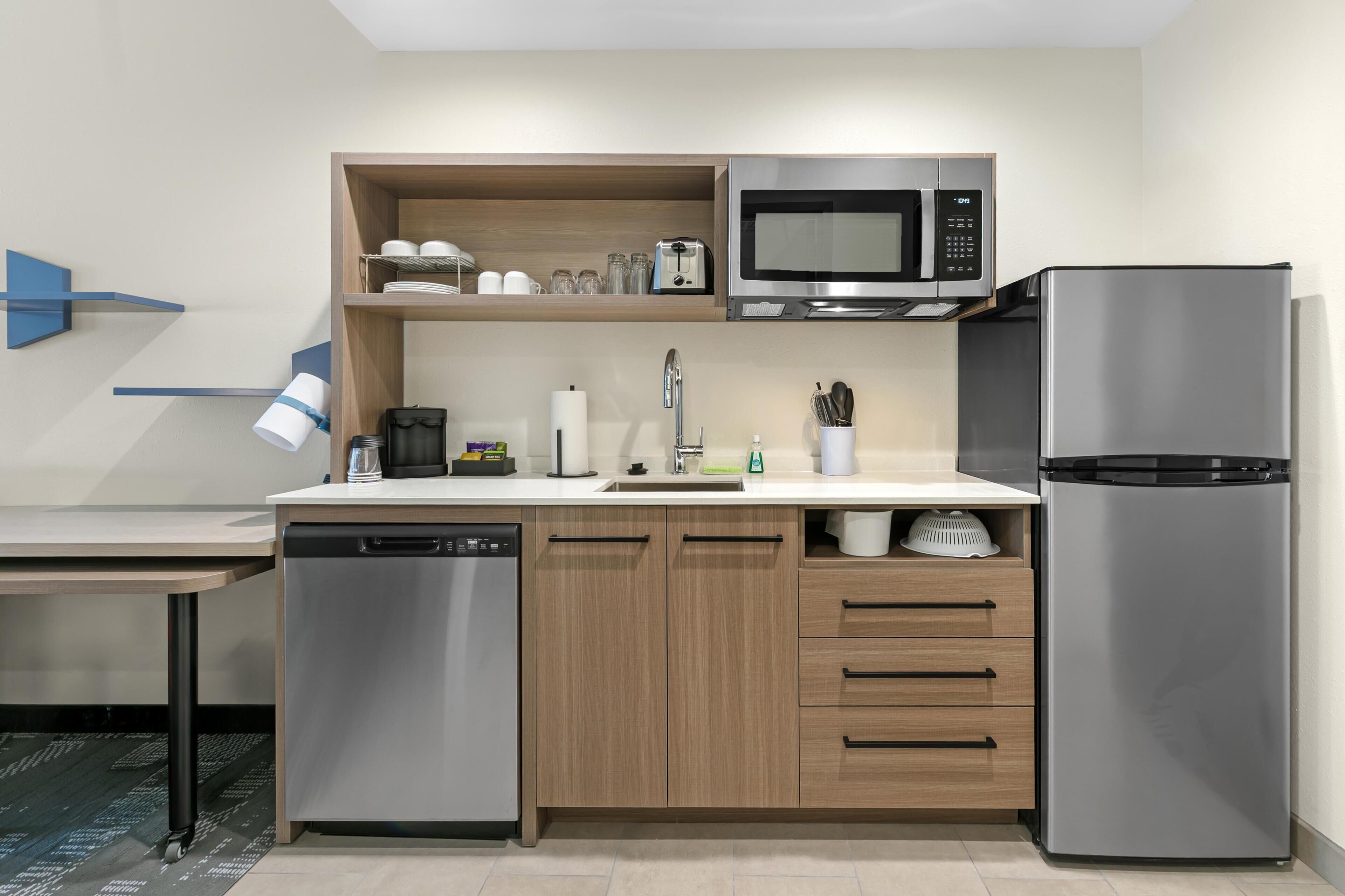 Eine moderne Küche mit Geschirrspüler, Mikrowelle, Kühlschrank, Holzschränken und einer Spüle.