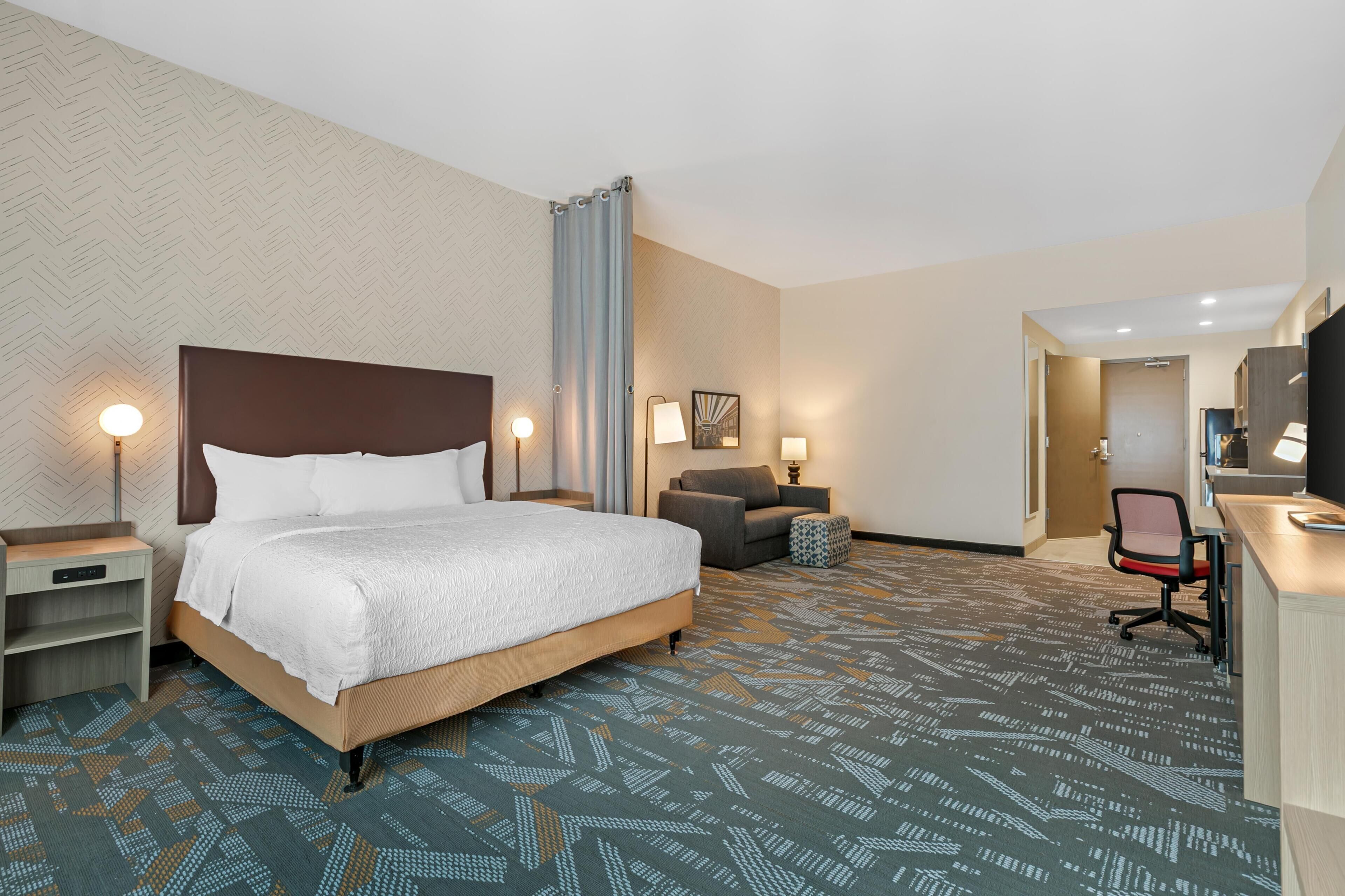 A hotel room with a bed, desk, chair, and a patterned carpet.