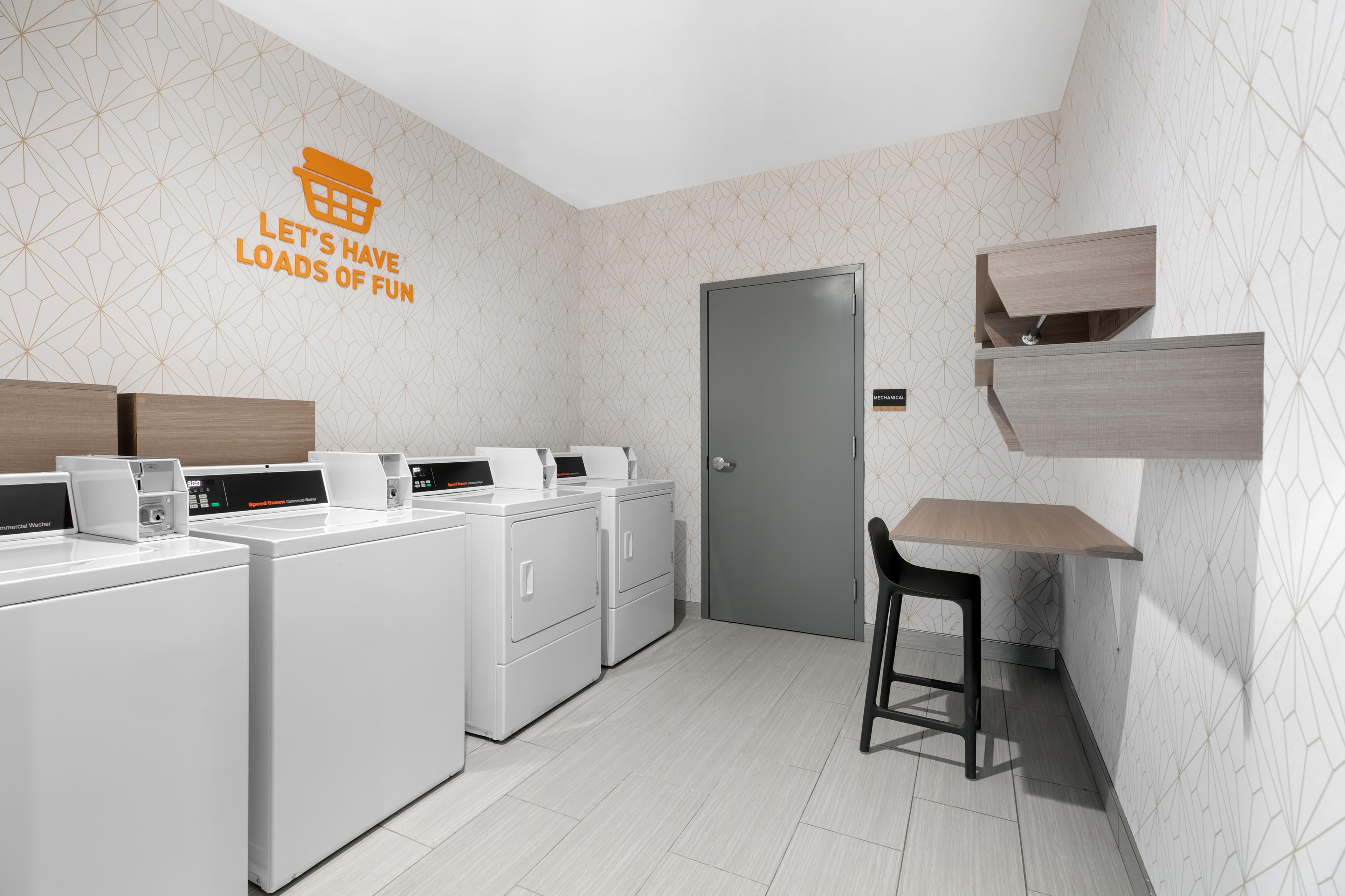Uma lavanderia moderna com uma placa na parede, uma porta e uma pequena mesa com uma cadeira.