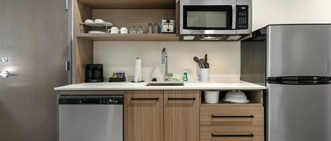 A modern kitchen with a dishwasher, microwave, refrigerator, wooden cabinets, and a sink.