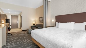 Ein Hotelzimmer mit einem großen Bett, einem Schreibtisch mit Stuhl, einer Couch und einem Fernseher.