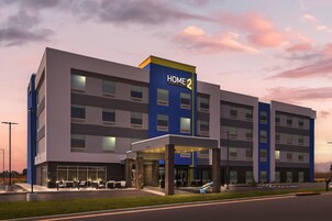 Un hotel de varios pisos con un llamativo letrero 'HOME 2', asientos exteriores y una entrada bien iluminada.