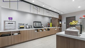 Ein moderner Hotel-Empfangsbereich mit Selbstbedienungsbereich, einer Kaffeemaschine und einer Obstauslage.