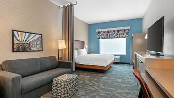 Une chambre d’hôtel avec un lit, un canapé, une télévision, un bureau et une moquette à motifs.