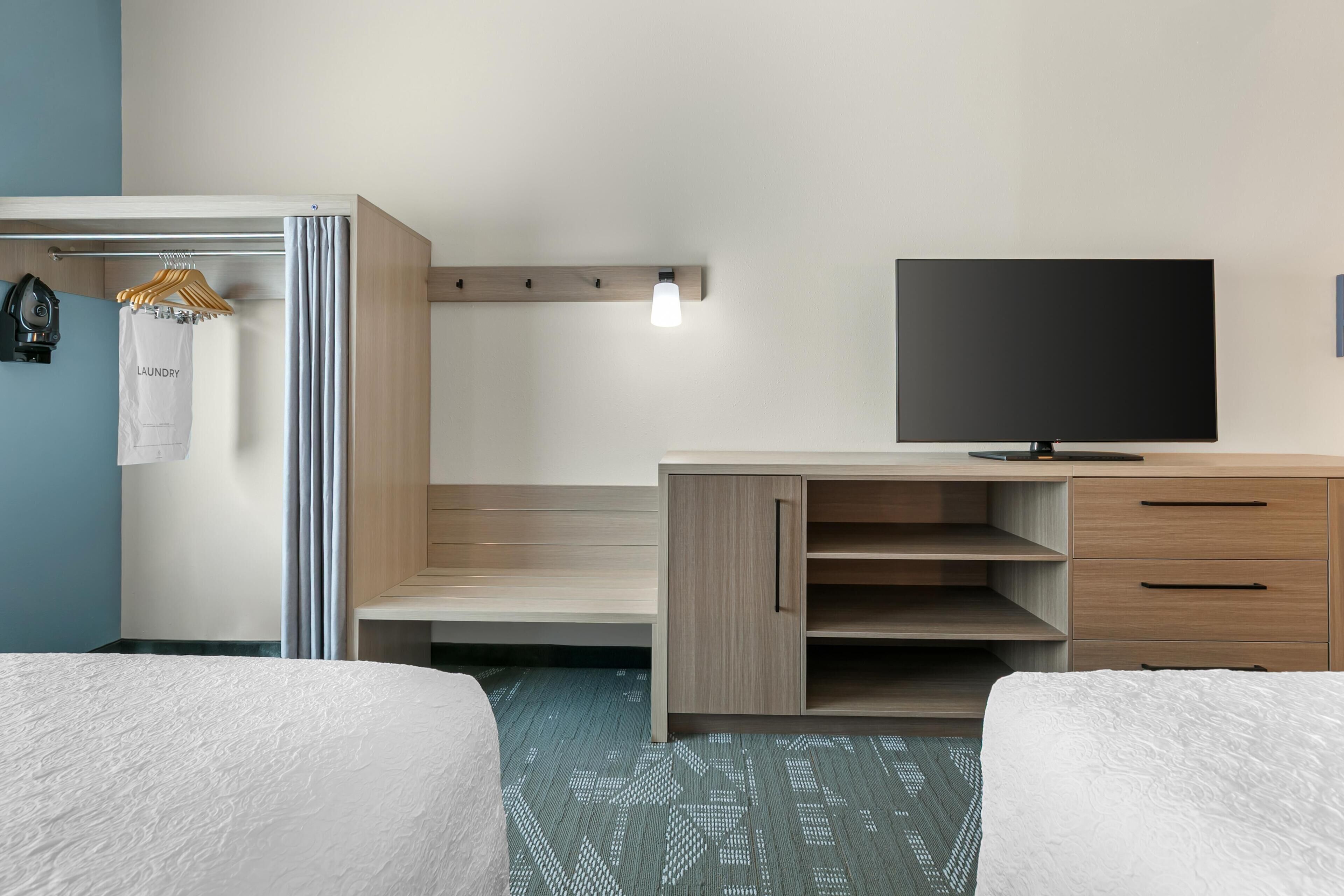 A hotel room with two beds, a TV, a wardrobe, and a light fixture.