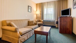 A hotel room with a sofa, a small table, a TV on a wooden cabinet, and a window with curtains. - Comfort Inn & Suites Shawinigan (Shawinigan)