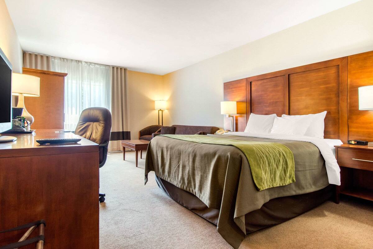 A hotel room with a large bed, a desk, a chair, and two bedside lamps.
