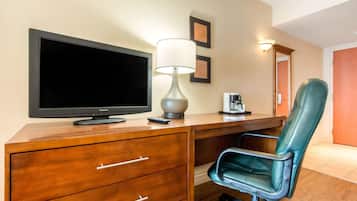 A hotel room with a wooden desk, a flat-screen TV, a lamp, a leather chair, and a coffee maker.