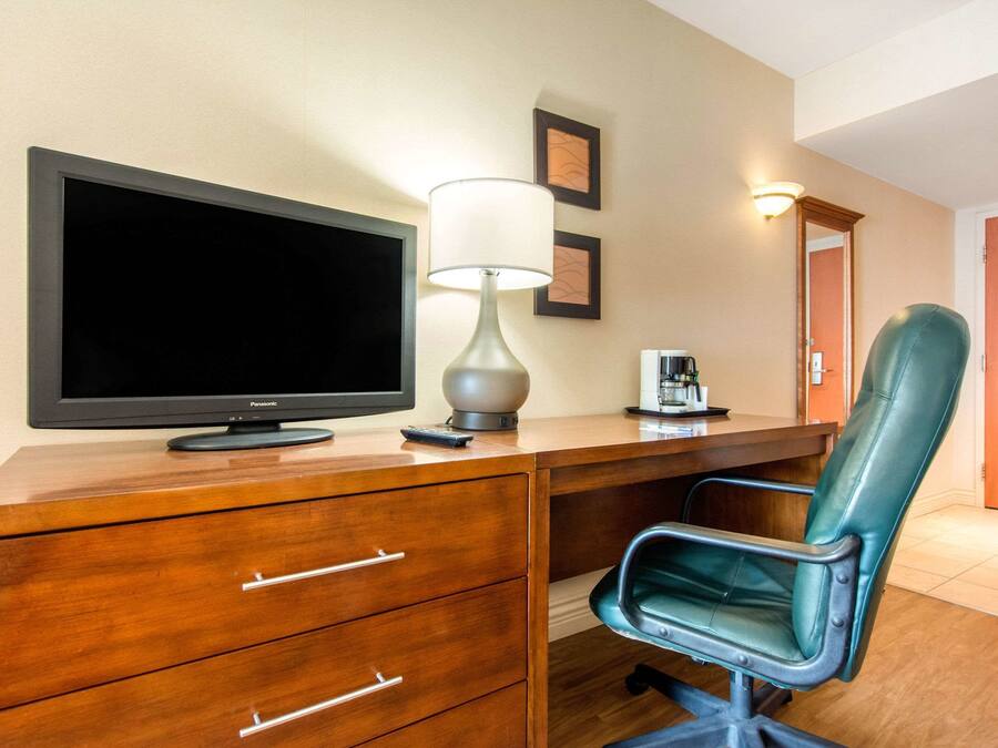A hotel room with a wooden desk, a flat-screen TV, a lamp, a leather chair, and a coffee maker.