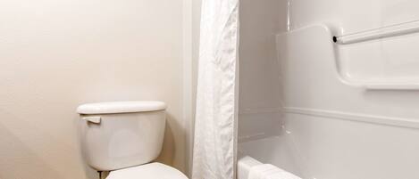 Une salle de bain comprenant des toilettes, une douche avec un rideau blanc et une baignoire avec un porte-serviettes.