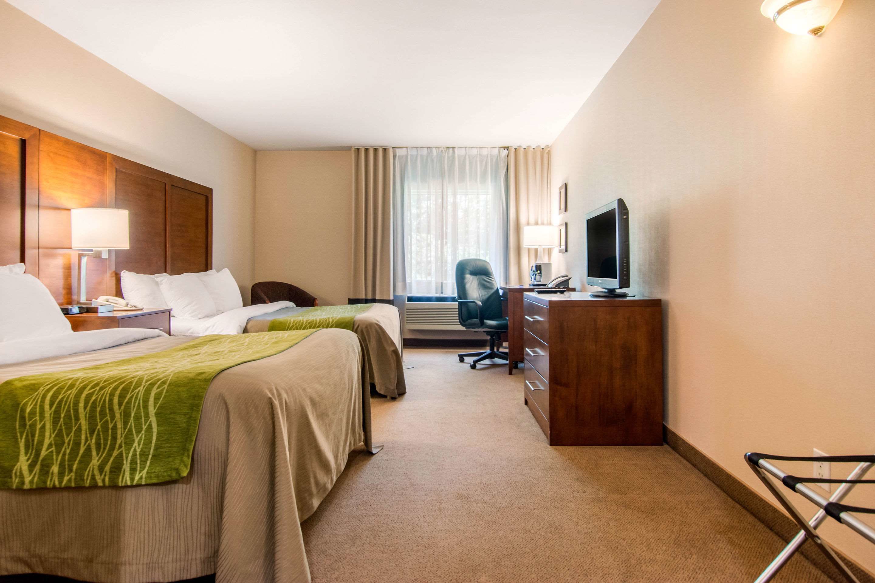 A hotel room with two beds, a desk, a chair, a television, and a window with curtains.