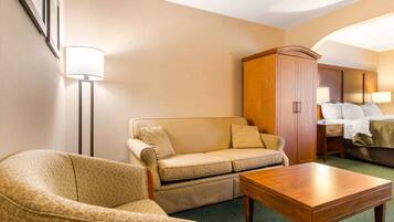 A hotel room with a sofa, armchair, wooden table, and a cabinet.