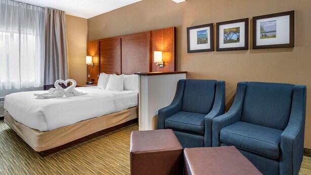A hotel room with a bed, two armchairs, a small table, and three framed pictures on the wall. - Comfort Suites Elkhart North (Elkhart)