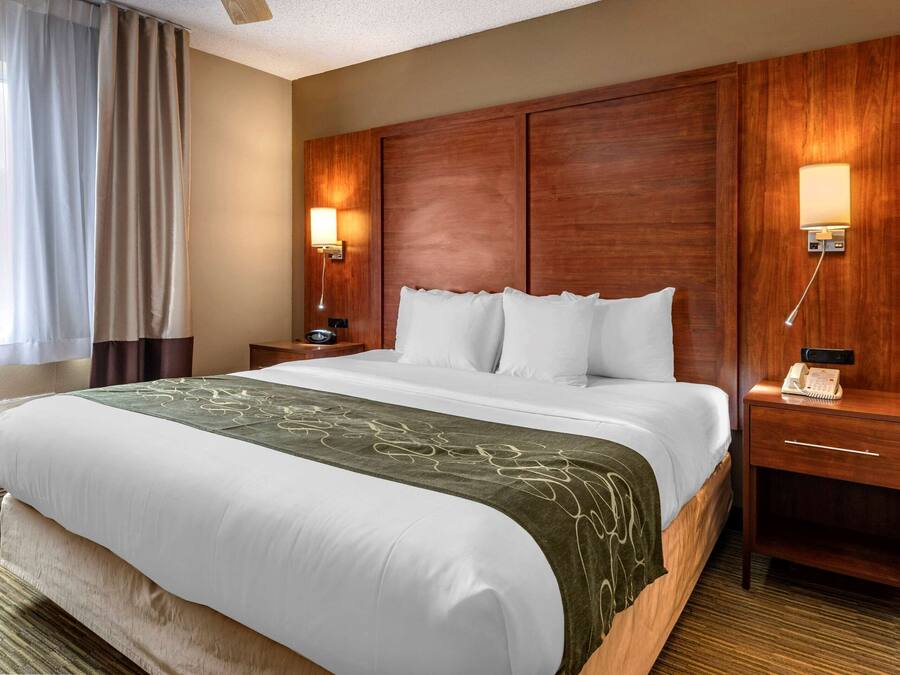 Habitación de hotel con una cama grande, cabecera de madera, lámparas de noche, un teléfono y una ventana con cortinas.
