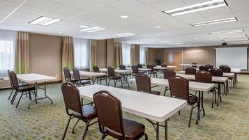 A conference room with multiple tables and chairs, large windows with curtains, and a projector screen.
