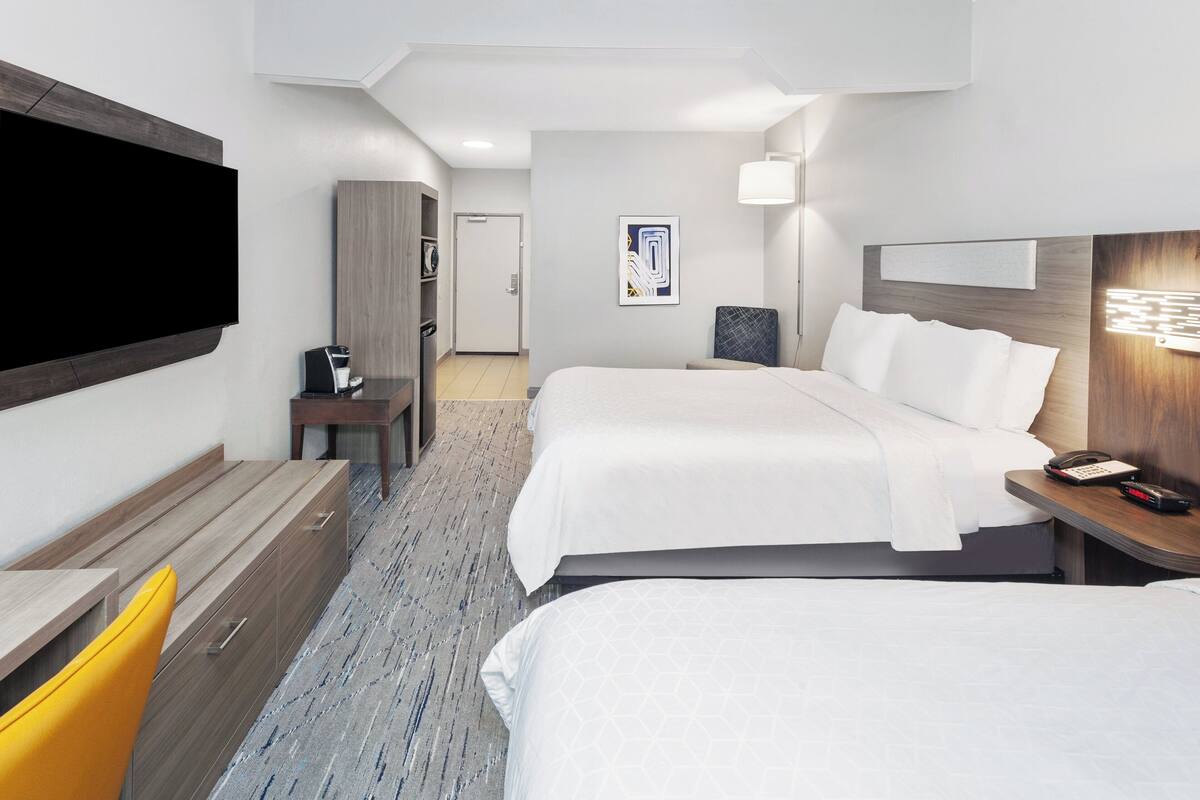 A hotel room with two beds, a desk, a TV, and a bathroom.