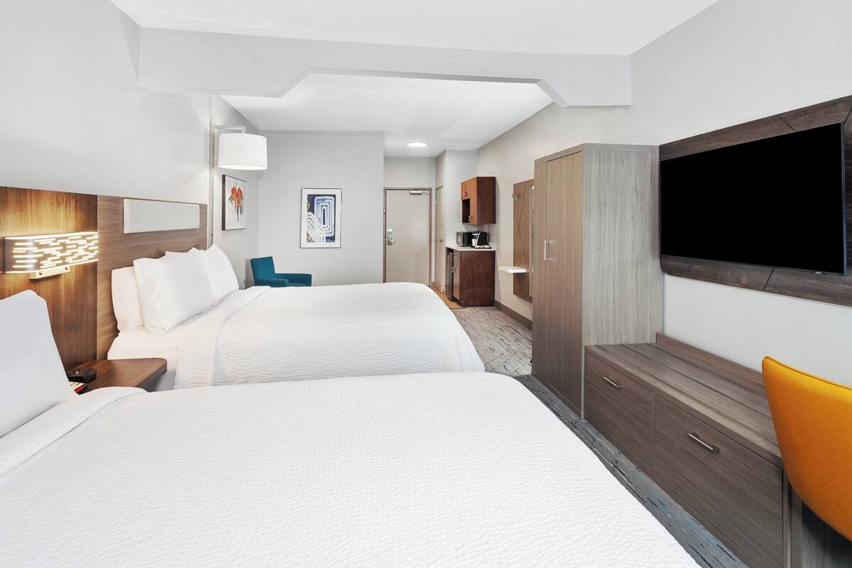 A hotel room with two beds, a TV, a wardrobe, and a desk with a lamp.