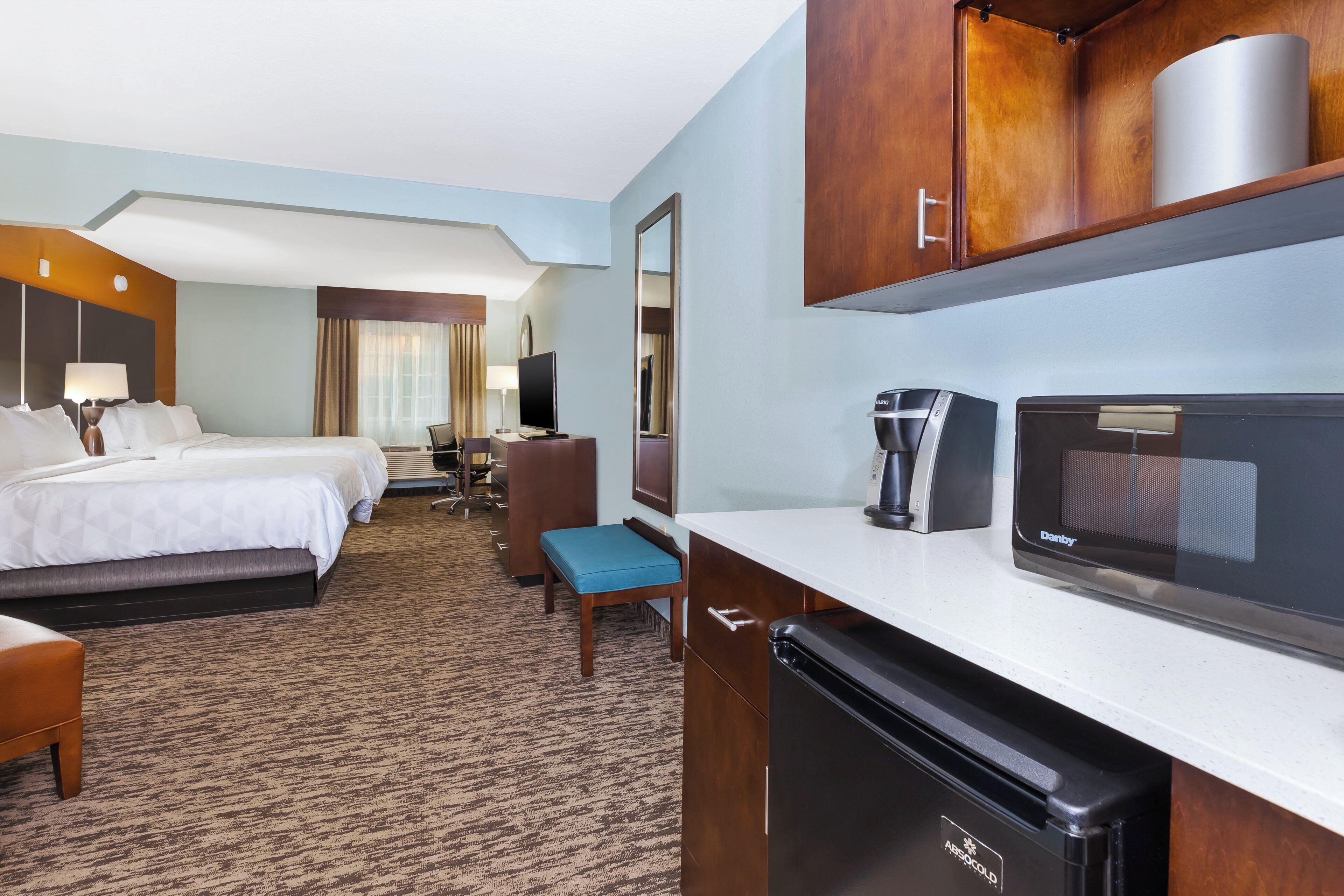 Una habitación de hotel con una cama, un escritorio con computadora, una cafetera y un microondas.
