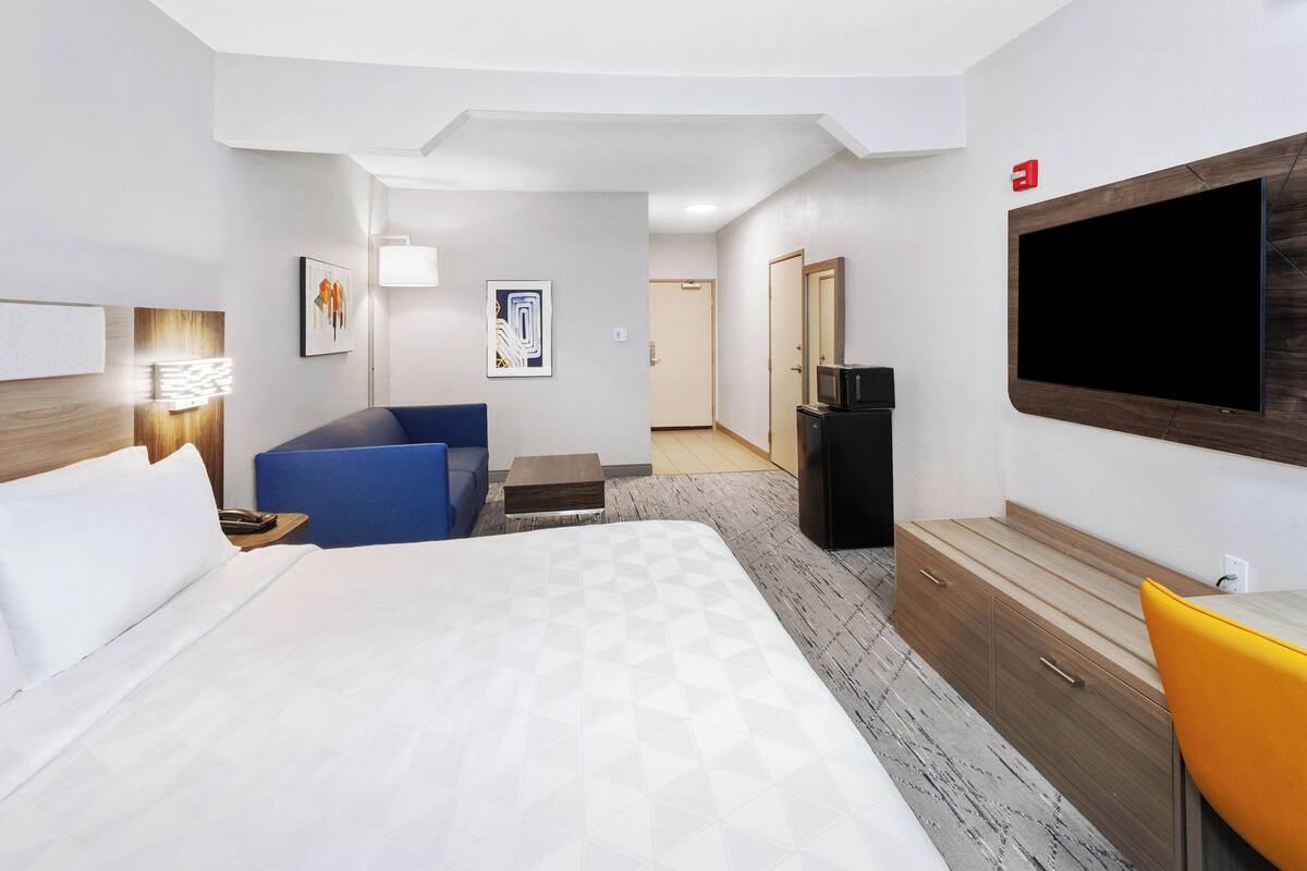 A hotel room with a large bed, a desk, a chair, a TV, and a wardrobe.