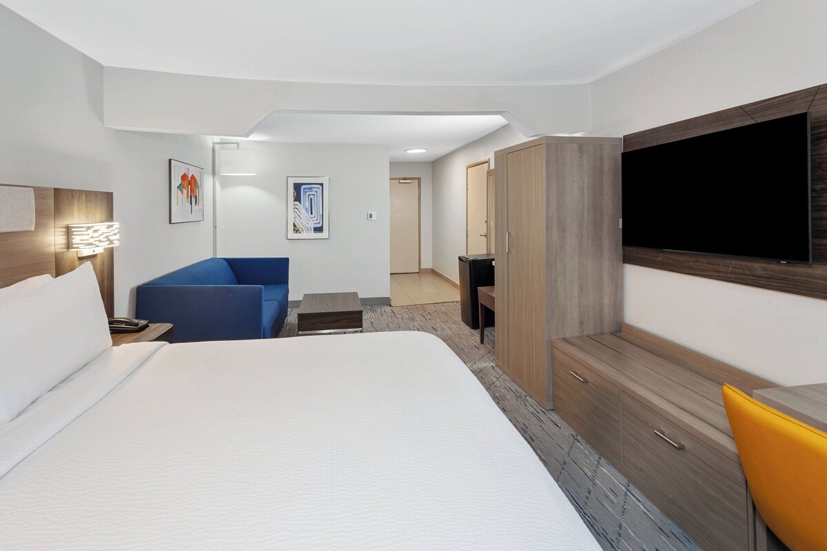 Une chambre d’hôtel avec un grand lit, un canapé bleu, une armoire en bois, un téléviseur à écran plat et une petite table.