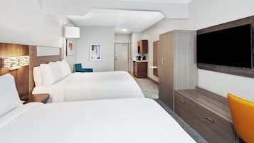 Una habitación de hotel con dos camas, televisión, armario y escritorio con lámpara.