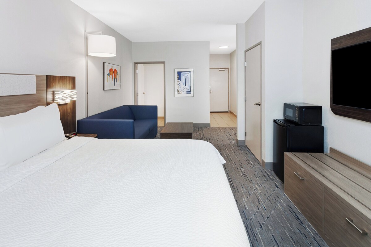Une chambre d’hôtel avec un grand lit, un canapé bleu, un téléviseur à écran plat, un four à micro-ondes et une commode en bois.