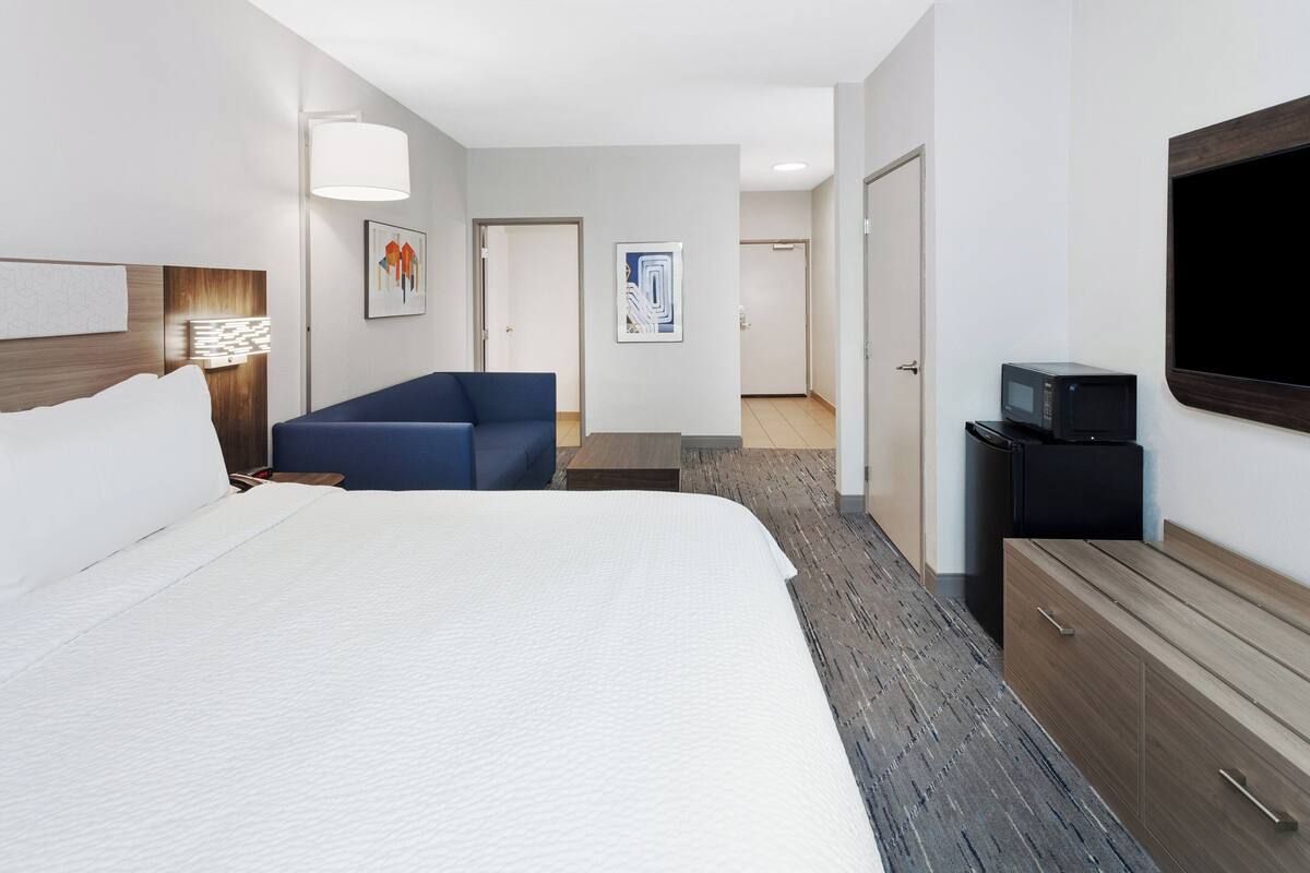 A hotel room with a large bed, a blue sofa, a flat-screen TV, a microwave, and a wooden dresser.