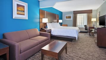 Habitación de hotel con cama, sofá, escritorio, televisor y ventana con cortinas.