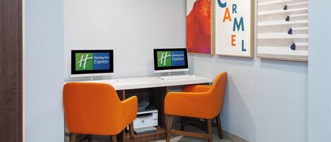 A hotel room with two orange chairs, a white desk, two monitors, and a printer.