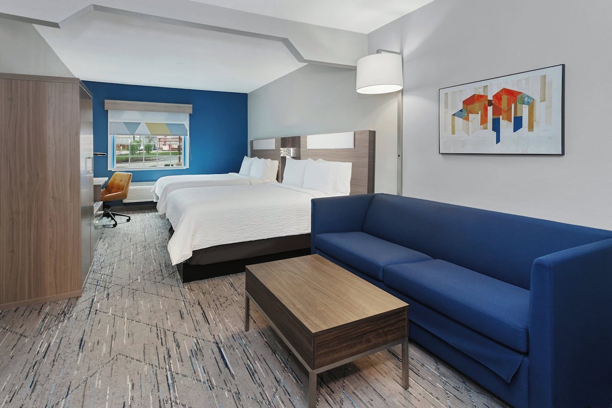 A hotel room with a bed, a blue sofa, a wooden coffee table, and a desk with a chair.
