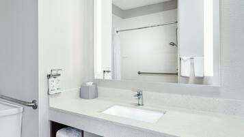 A modern bathroom with a white sink, a mirror, and a shower area.