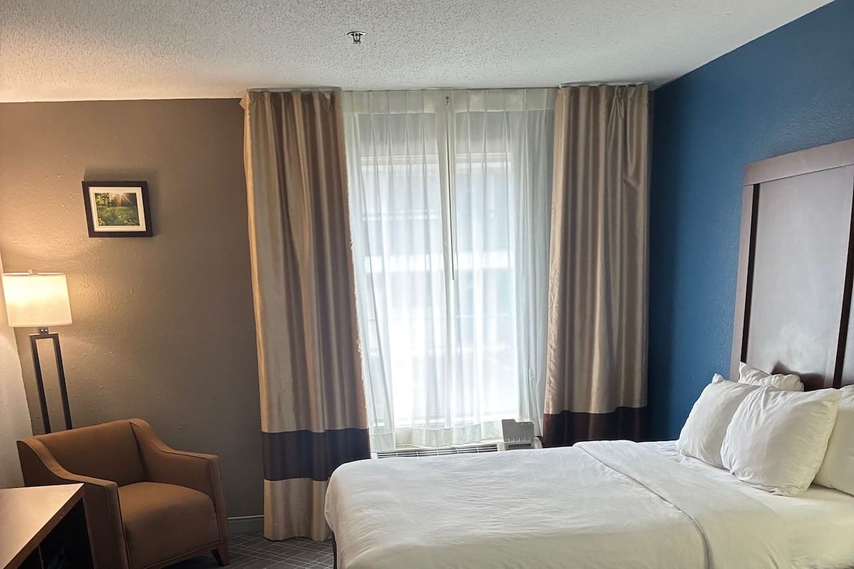 A hotel room with two beds, a desk, a chair, and a lamp.
